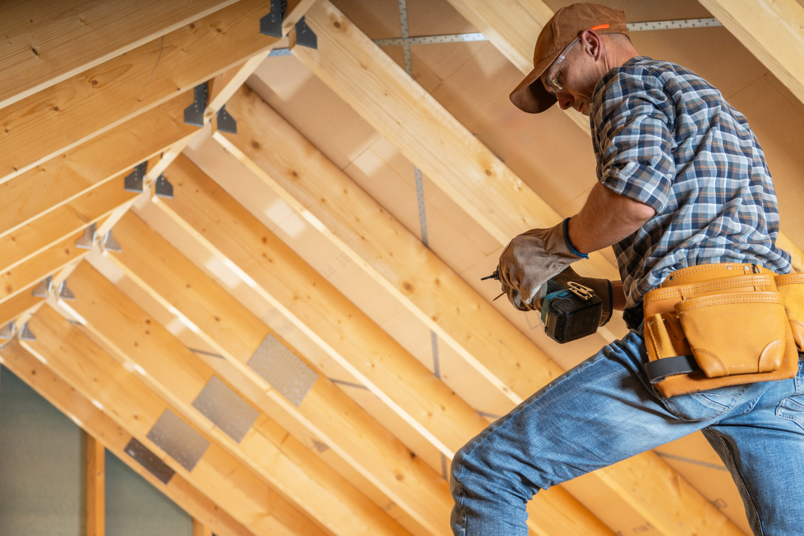 Minnesota Carpentry contractor using a power drill in a residential attic, showcasing Can Do Insurance protection for builders and construction projects.